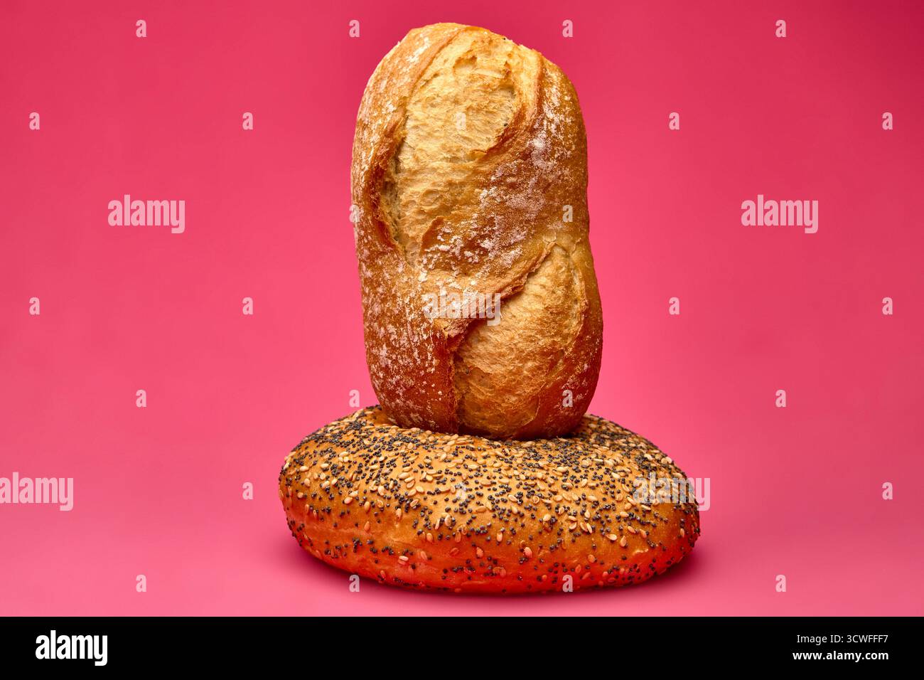 Panino verticale posizionato in posizione verticale sopra un panino con semi di papavero su sfondo rosa. Composizione unica degli alimenti da studio che simboleggia l'equilibrio e la creatività Foto Stock