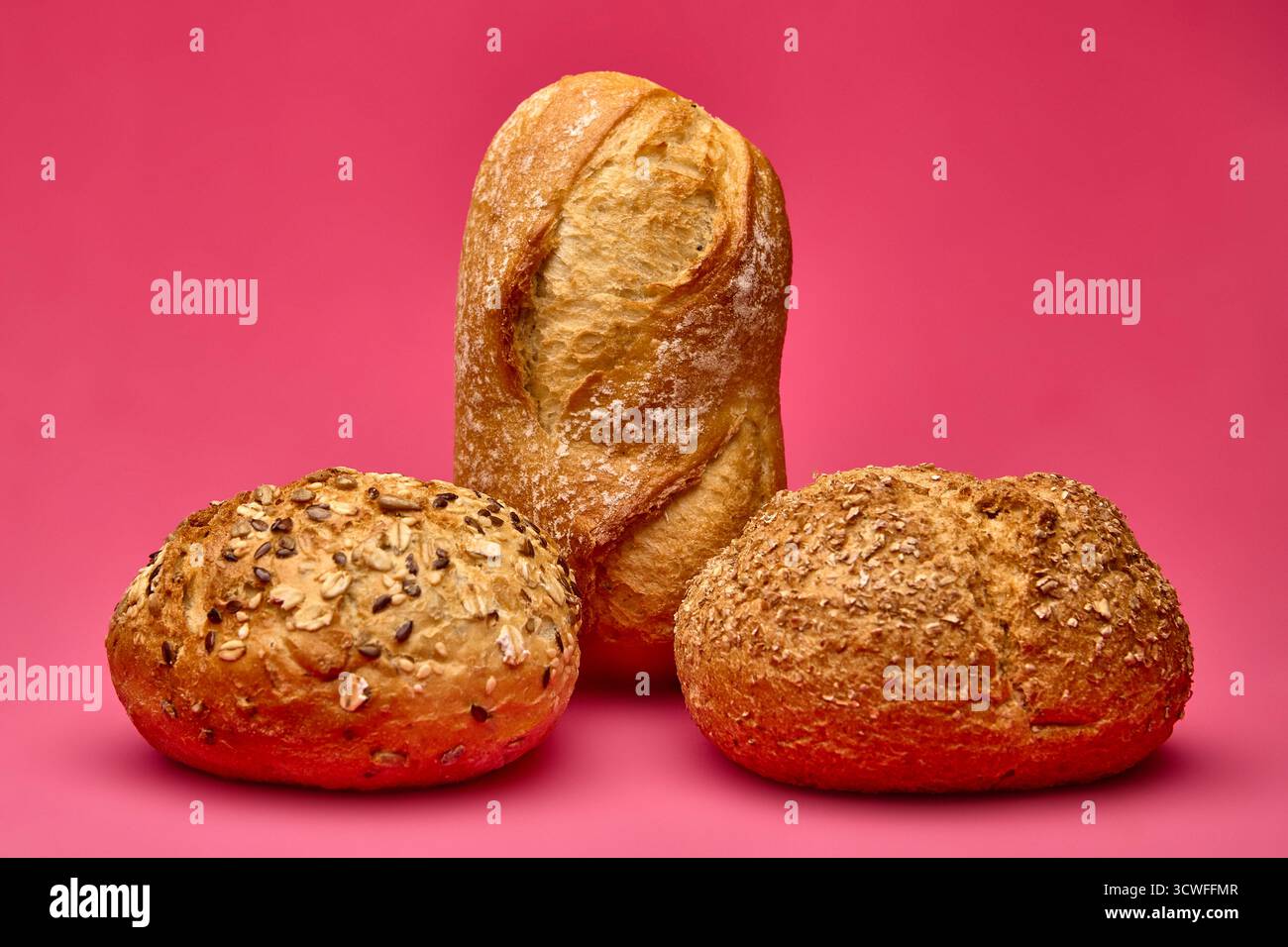 Pane verticale bilanciato su due panini rotondi su sfondo rosa. Composizione concettuale del cibo che simboleggia l'equilibrio e la creatività nel fotogra da forno Foto Stock