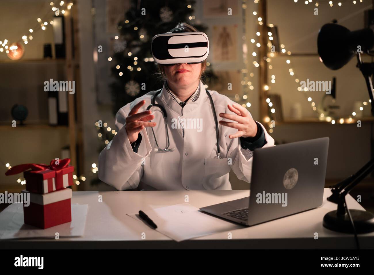 La giovane dottoressa indossa il cappello di Babbo Natale e gli occhiali vr che guardano la realtà metaversa durante il turno di lavoro la sera della vigilia di Natale. Medicina, santo Foto Stock