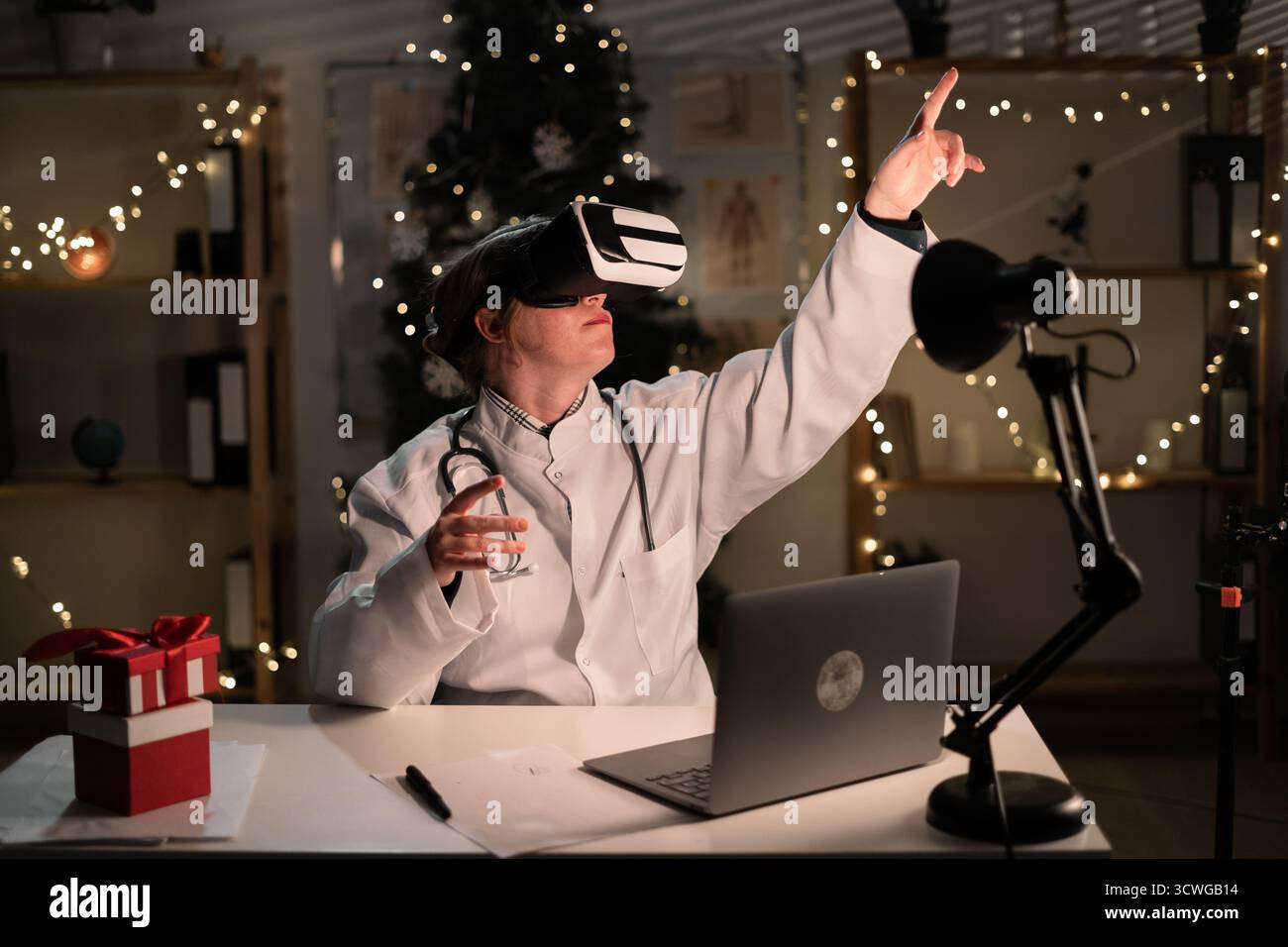 La giovane dottoressa indossa il cappello di Babbo Natale e gli occhiali vr che guardano la realtà metaversa durante il turno di lavoro la sera della vigilia di Natale. Medicina, vacanze, Foto Stock