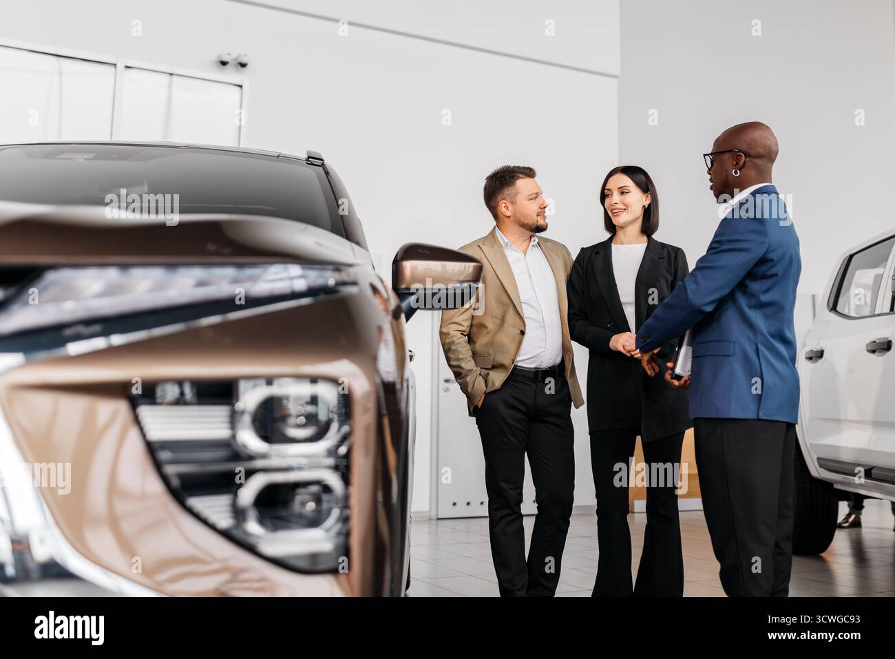 Gruppi diversi di persone che discutono delle opzioni dei veicoli presso una concessionaria, con le vetture in background, sottolineando l'importanza del motore del cliente Foto Stock