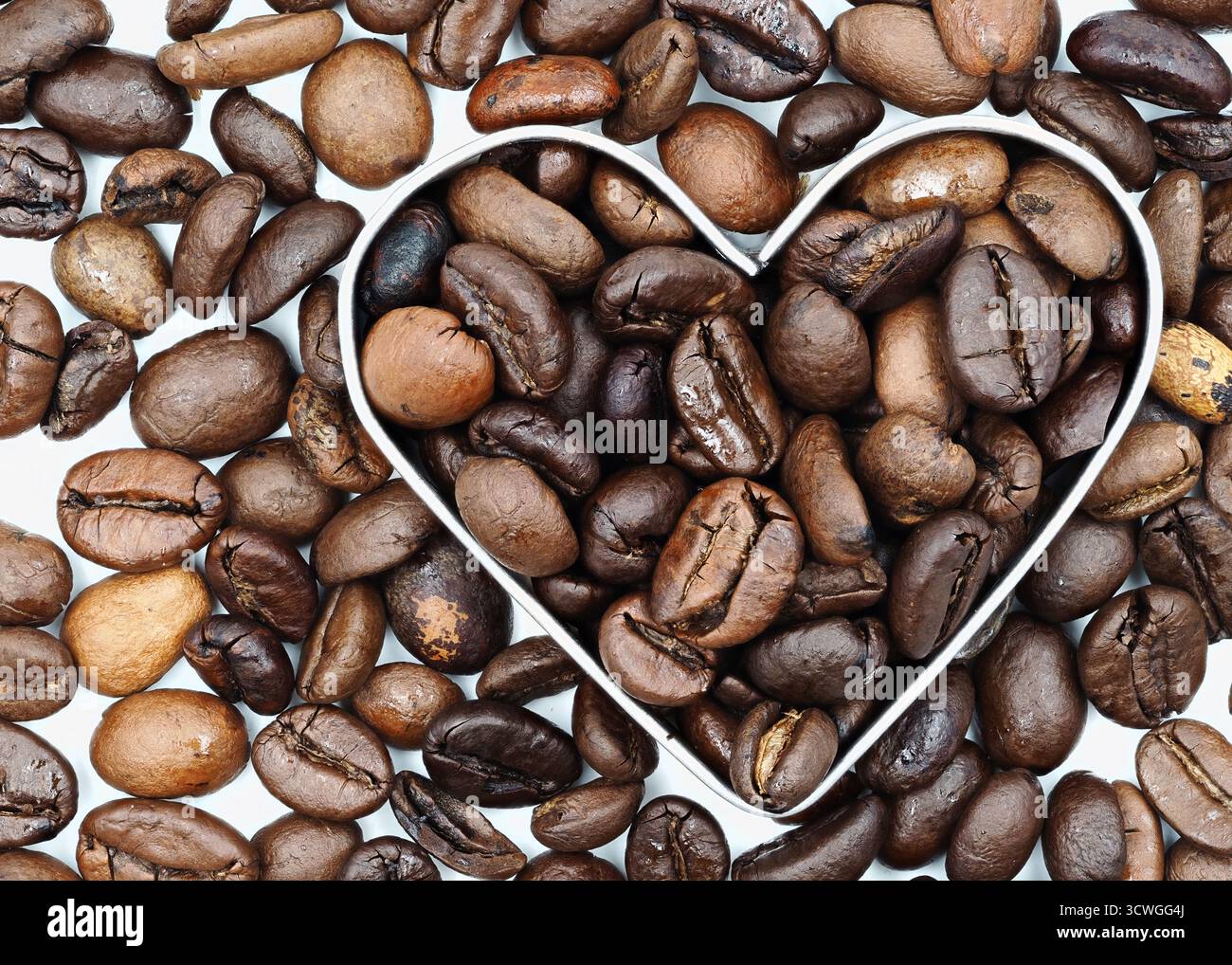 Vari chicchi di caffè sono disposti artisticamente per formare una forma a cuore, sottolineando la bellezza e la ricchezza del caffè. Questo display cattura l'essenza Foto Stock