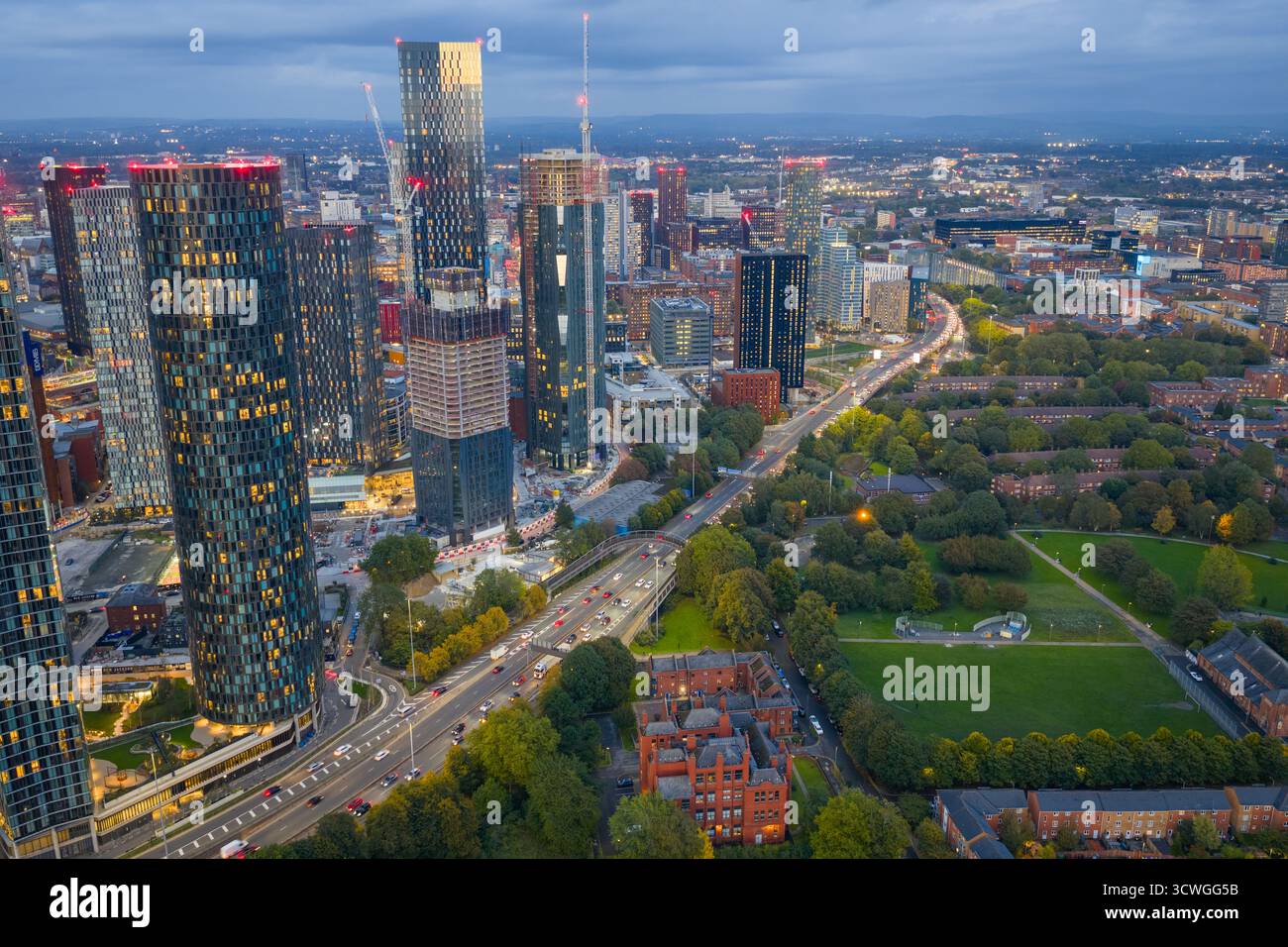 Immagine aerea al crepuscolo dello skyline di Manchester con grattacieli illuminati e la via mancuniana sottostante. Foto Stock