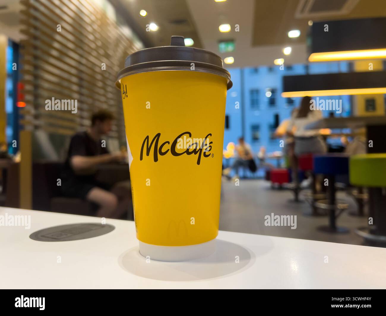 Poznan, Polonia - 11 settembre 2025: Tazza gialla con marchio McCafe con coperchio scuro sul bancone bianco, che riflette le popolari bevande del McDonald's Cafe accessibili Foto Stock