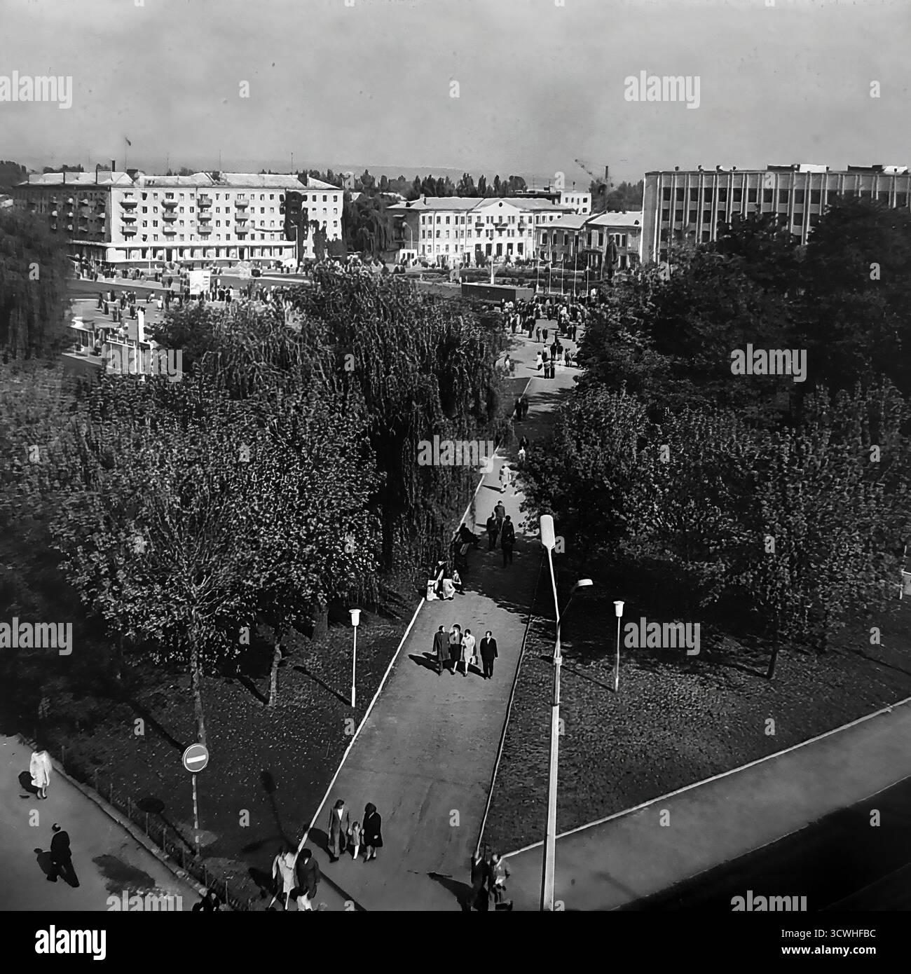 Una vista panoramica ad alto angolo cattura un enorme raduno pubblico in Piazza della Rivoluzione d'ottobre (ora Piazza Soborna) a Sloviansk, RSS Ucraina, durante una vacanza in tutta la città negli anni '1970 Folle di persone riempiono la piazza centrale e i vicoli circostanti, con l'importante monumento di Lenin al suo cuore. Fiancheggiata dall'edificio del Consiglio comunale e dai blocchi residenziali, la scena è un potente documento della vita comunitaria, delle riunioni sociali e delle celebrazioni statali in una tipica città provinciale sovietica durante l'era Brezhnev Foto Stock