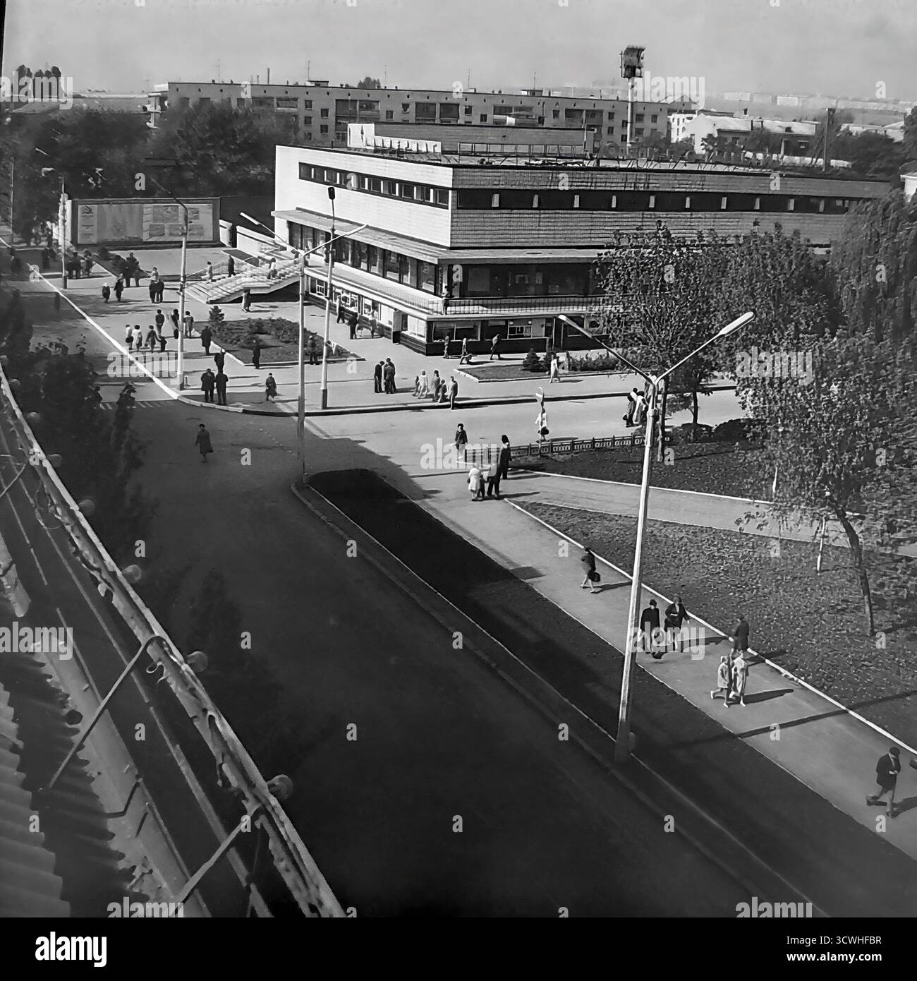 Una vista ad alto angolo cattura il grande magazzino centrale ("Univermag") e la vivace Piazza della Rivoluzione d'ottobre (ora Piazza Soborna) a Sloviansk, RSS Ucraina, durante gli anni '1970 L'edificio è un classico esempio di architettura modernista sovietica, che funge da principale centro commerciale della città. I pedoni passeggiano lungo gli ampi marciapiedi e la piazza, mostrando la vita quotidiana e l'ambiente urbano di una tipica città provinciale dell'URSS durante l'era Brezhnev. Questa foto in bianco e nero evoca un forte senso di nostalgia per il periodo Foto Stock