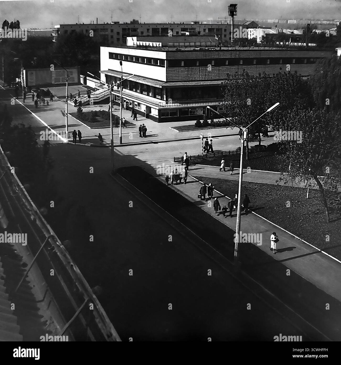 Una vista ad alto angolo cattura il grande magazzino centrale ("Univermag") e la vivace Piazza della Rivoluzione d'ottobre (ora Piazza Soborna) a Sloviansk, RSS Ucraina, durante gli anni '1970 L'edificio è un classico esempio di architettura modernista sovietica, che funge da principale centro commerciale della città. I pedoni passeggiano lungo gli ampi marciapiedi e la piazza, mostrando la vita quotidiana e l'ambiente urbano di una tipica città provinciale dell'URSS durante l'era Brezhnev. Questa foto in bianco e nero evoca un forte senso di nostalgia per il periodo Foto Stock
