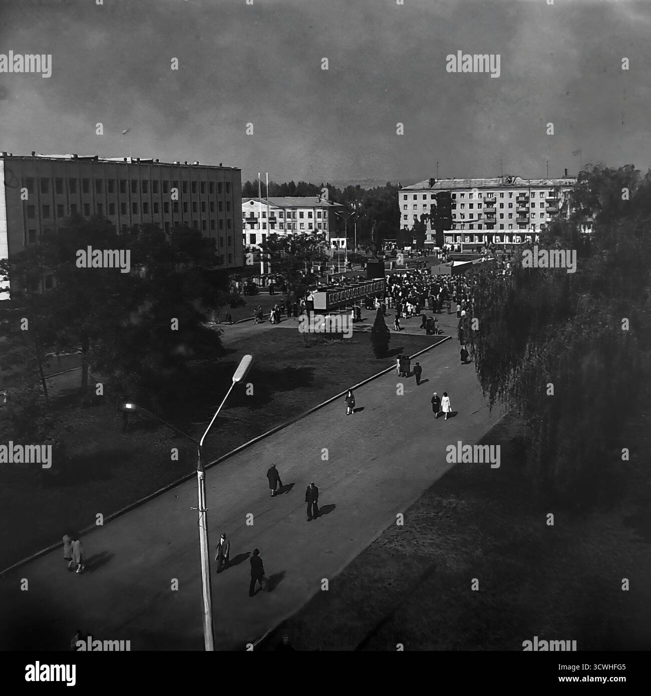 Una vista panoramica ad alto angolo cattura un enorme raduno pubblico in Piazza della Rivoluzione d'ottobre (ora Piazza Soborna) a Sloviansk, RSS Ucraina, durante una vacanza in tutta la città negli anni '1970 Folle di persone riempiono la piazza centrale e i vicoli circostanti, con l'importante monumento di Lenin al suo cuore. Fiancheggiata dall'edificio del Consiglio comunale e dai blocchi residenziali, la scena è un potente documento della vita comunitaria, delle riunioni sociali e delle celebrazioni statali in una tipica città provinciale sovietica durante l'era Brezhnev Foto Stock