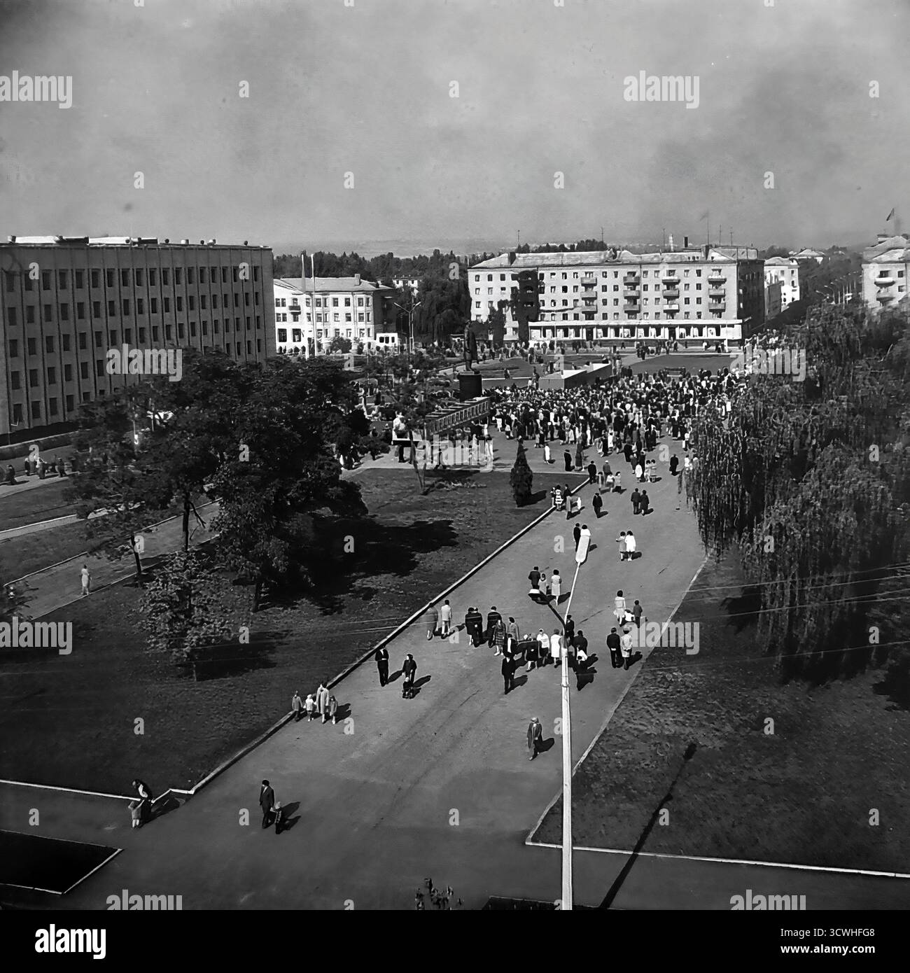 Una vista panoramica ad alto angolo cattura un enorme raduno pubblico in Piazza della Rivoluzione d'ottobre (ora Piazza Soborna) a Sloviansk, RSS Ucraina, durante una vacanza in tutta la città negli anni '1970 Folle di persone riempiono la piazza centrale e i vicoli circostanti, con l'importante monumento di Lenin al suo cuore. Fiancheggiata dall'edificio del Consiglio comunale e dai blocchi residenziali, la scena è un potente documento della vita comunitaria, delle riunioni sociali e delle celebrazioni statali in una tipica città provinciale sovietica durante l'era Brezhnev Foto Stock