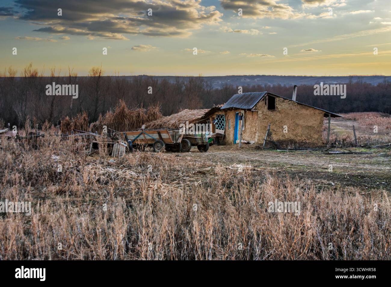 Povertà nel villaggio rurale rumeno, case di fango e carretto dei cavalli, erba secca e alberi in autunno, tramonto Foto Stock