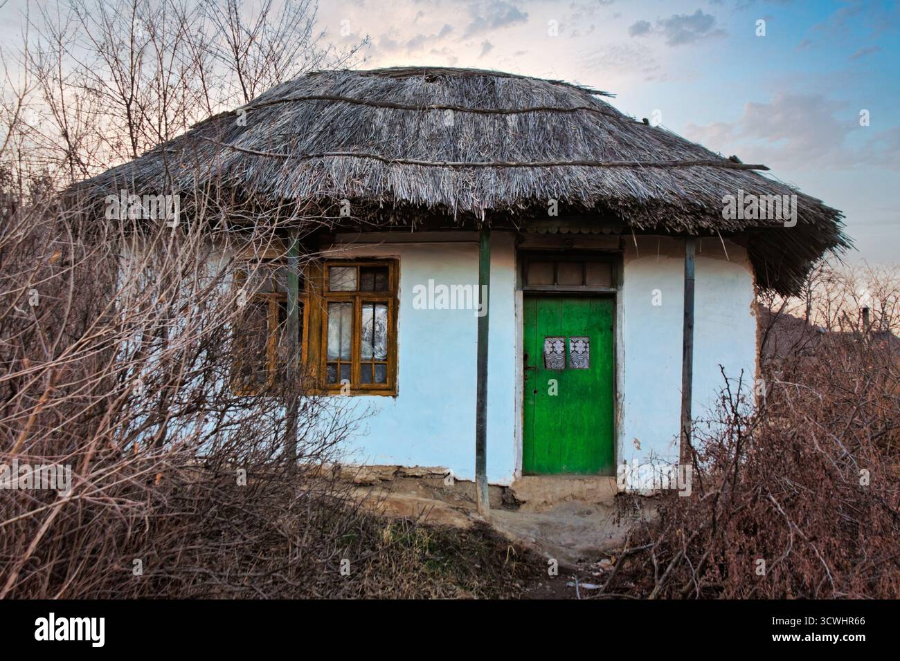 Povertà nel villaggio di campagna rumeno, casa di fango con tetto in paglia, erba secca e alberi in autunno, tramonto Foto Stock