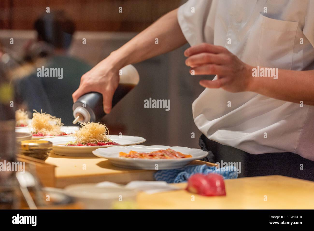 Lo chef prepara sapientemente piatti gourmet con attenzione ai dettagli in una cucina contemporanea, che mette in mostra arte culinaria e creatività. Foto Stock