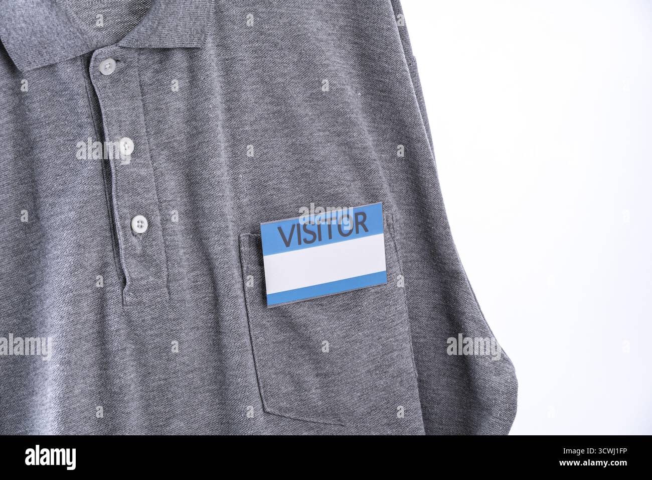 Camicia grigia con badge per visitatori in tasca, con design blu e bianco. la camicia è una polo casual che enfatizza l'aspetto professionale e rilassato Foto Stock
