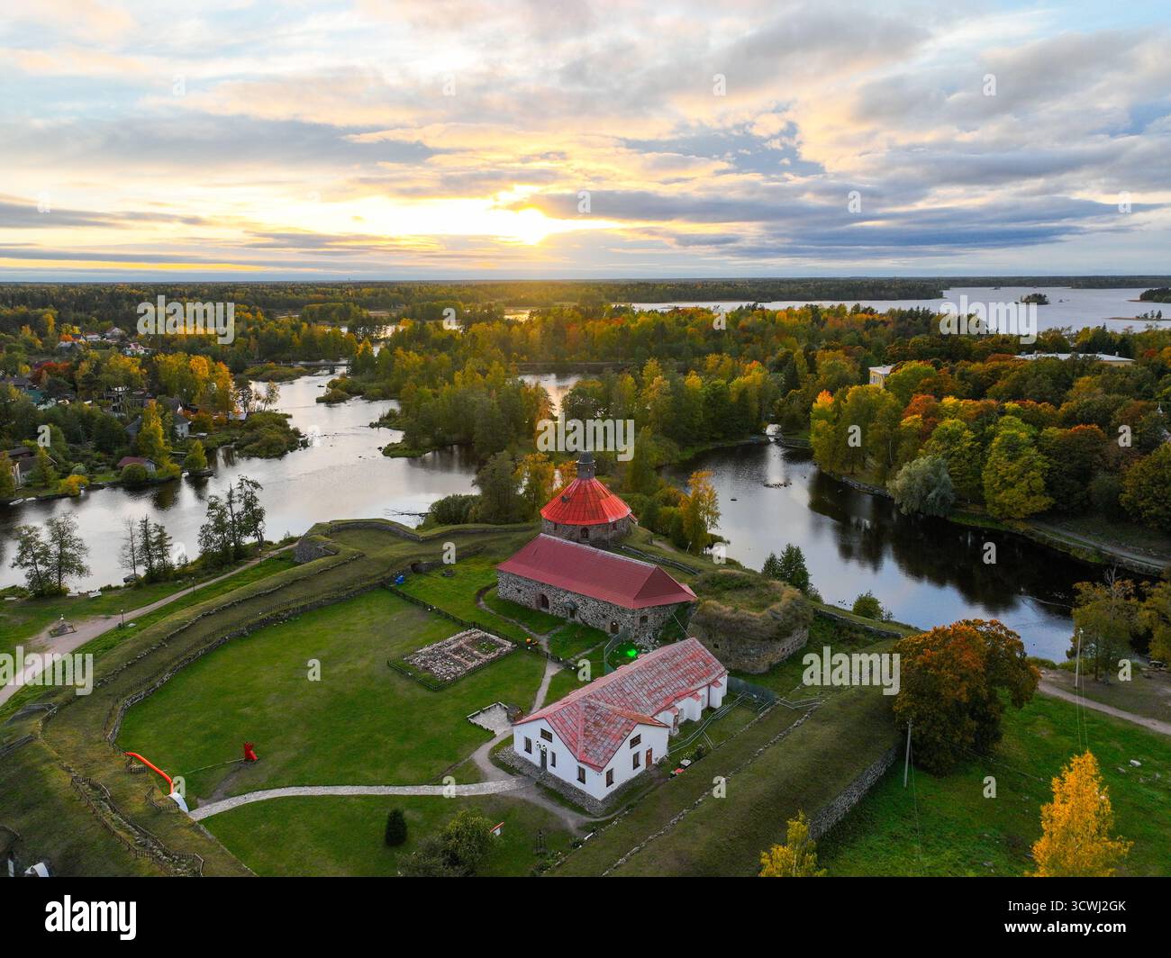 Vista aerea dei terreni della Fortezza di Korela su un'isola circondata da acqua e foresta autunnale al tramonto o all'alba con colori caldi del cielo Foto Stock