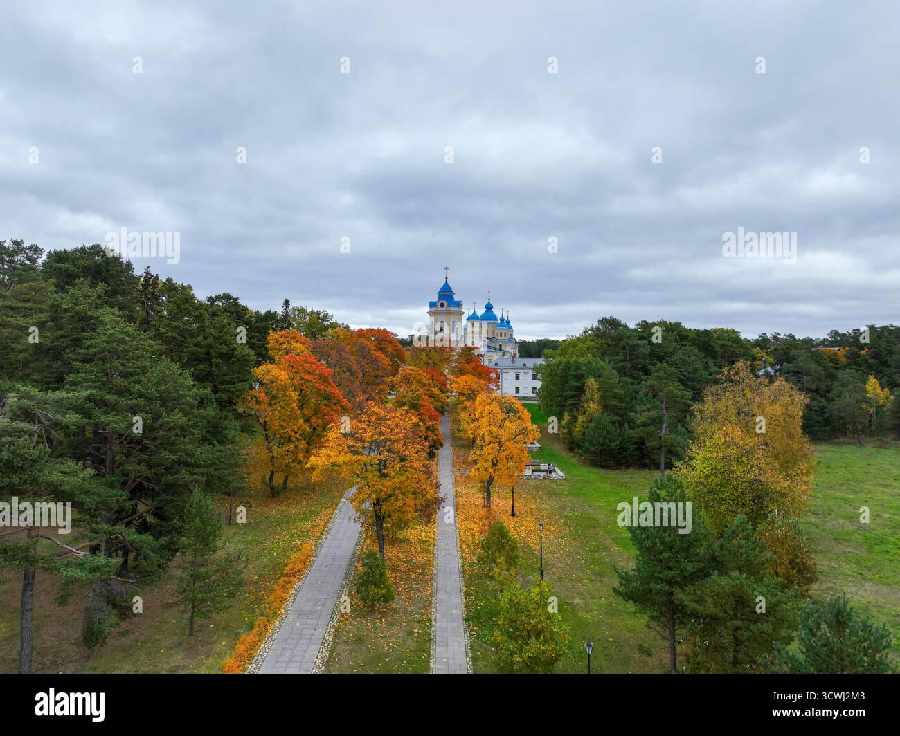 Veduta sopraelevata di un lungo viale alberato con fogliame autunnale arancione luminoso che conduce direttamente a una caratteristica chiesa a cupola bianca e blu Foto Stock