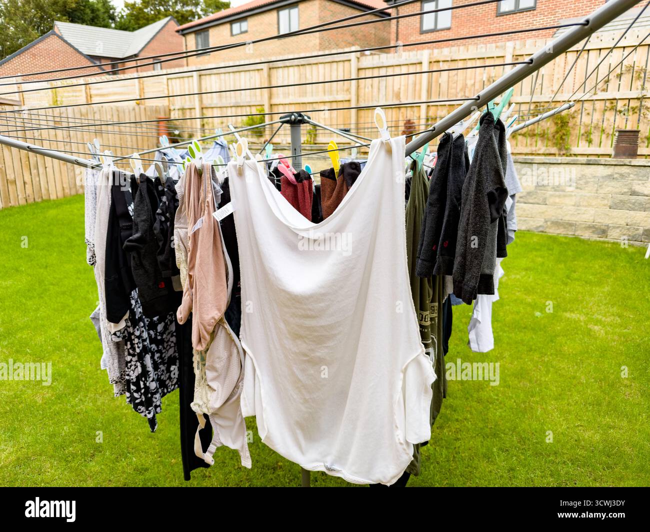 Vestiti colorati appesi su una linea di lavaggio rotante all'aperto in un cortile di periferia con un prato ben recintato nel regno unito Foto Stock