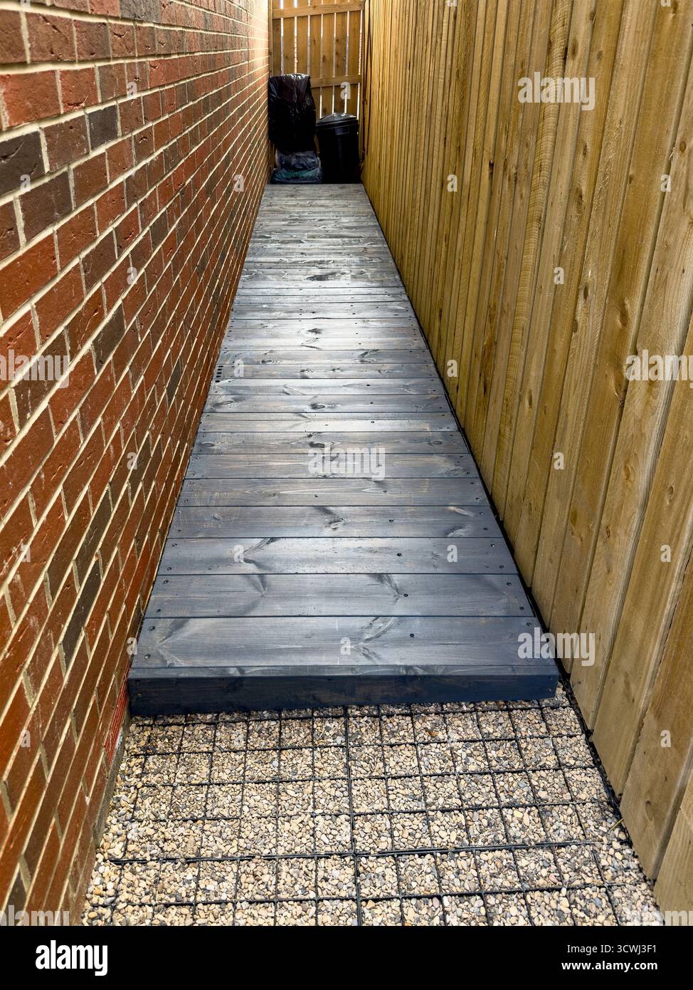 Stretto percorso del ponte in legno tra una parete in mattoni e una base di installazione per recinzione in legno per il progetto fai da te di capannoni - Immagine stock catturata con smartphone