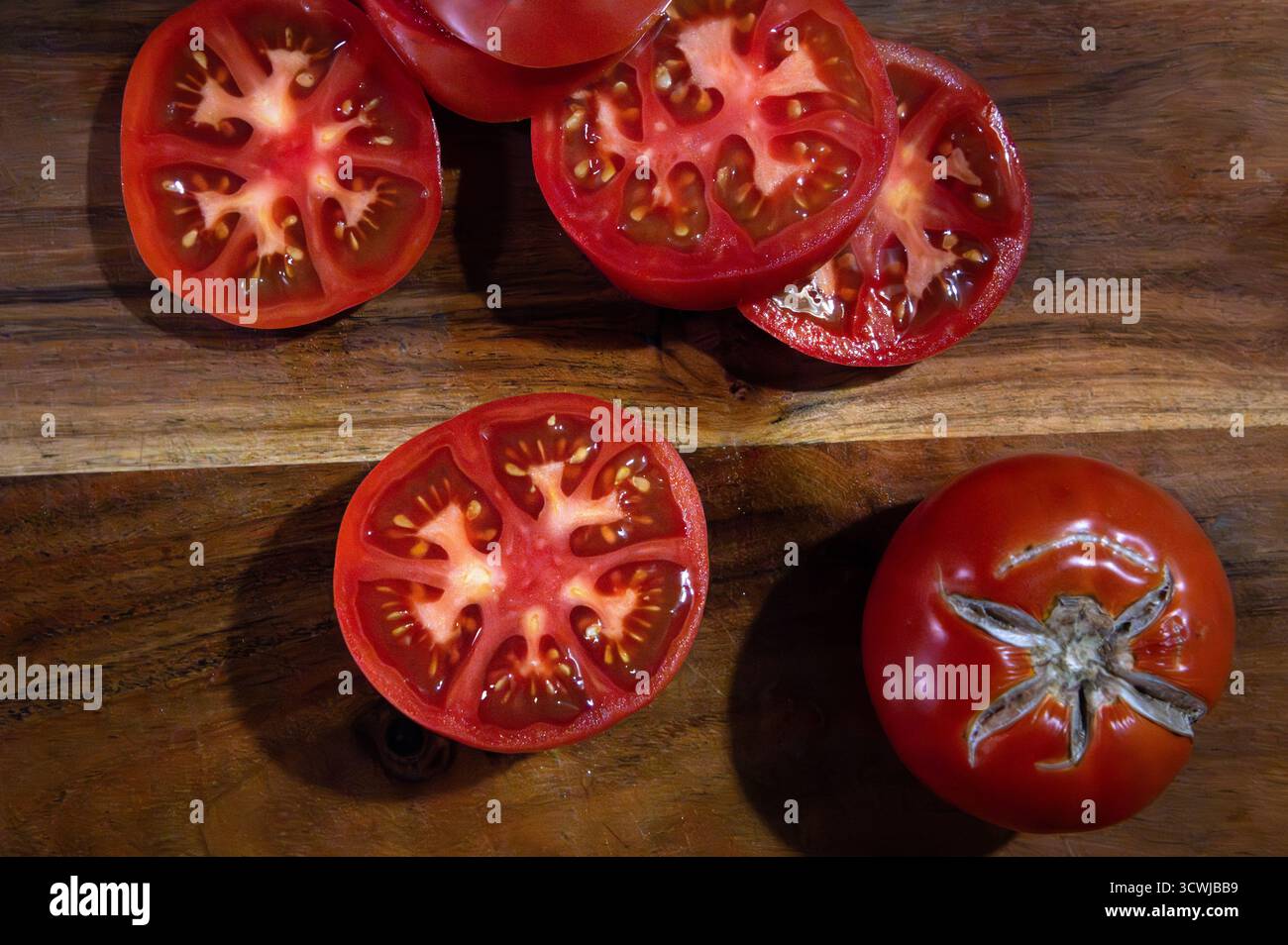 Un tagliere in legno con fette di pomodoro rosso maturo accanto a un pomodoro intero Foto Stock