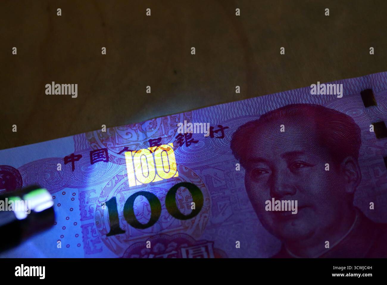 Primo piano di una banconota cinese da 100 Yuan sotto la luce UV, rivelando la funzione di sicurezza fluorescente con il numero luminoso 100. Foto Stock