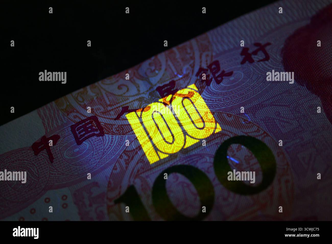 Primo piano di una banconota cinese da 100 Yuan sotto la luce UV, rivelando la funzione di sicurezza fluorescente con il numero luminoso 100. Foto Stock