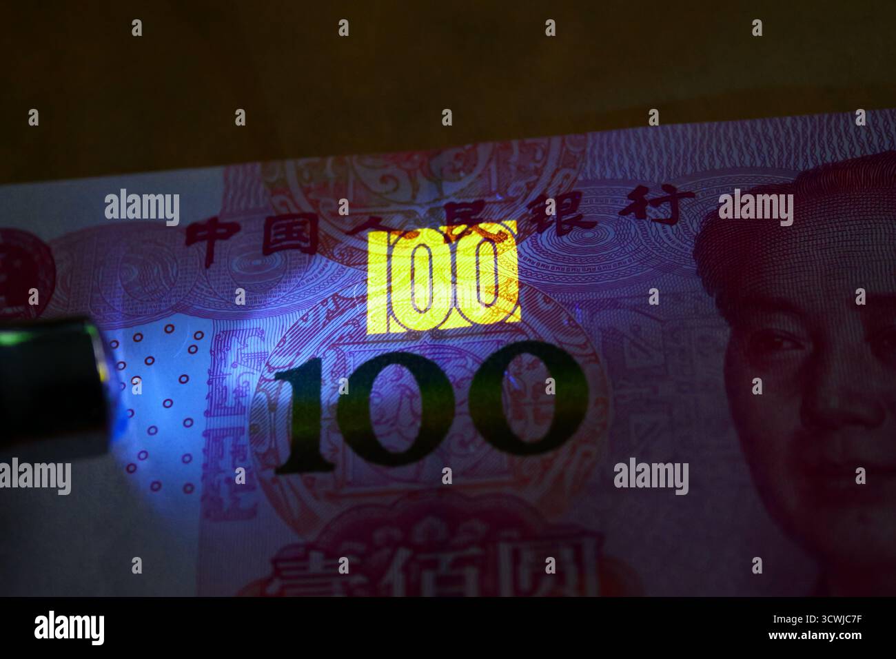 Primo piano di una banconota cinese da 100 Yuan sotto la luce UV, rivelando la funzione di sicurezza fluorescente con il numero luminoso 100. Foto Stock
