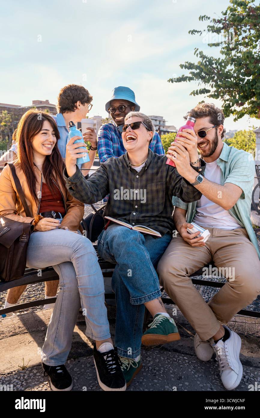 Ritratto sincero di un giovane e felice gruppo di amici che si diverte con bottiglie d'acqua in alluminio riutilizzabili in un parco al tramonto. Foto Stock