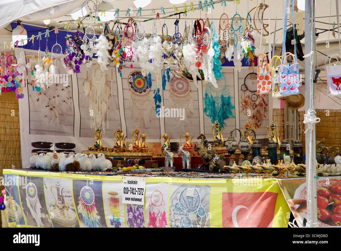 Un cartello bilingue per Hamdeok Seoubong Beach incorona uno stand di certificazione ciclistica rosso, con fronde di palme e il mare calmo sullo sfondo. Foto Stock