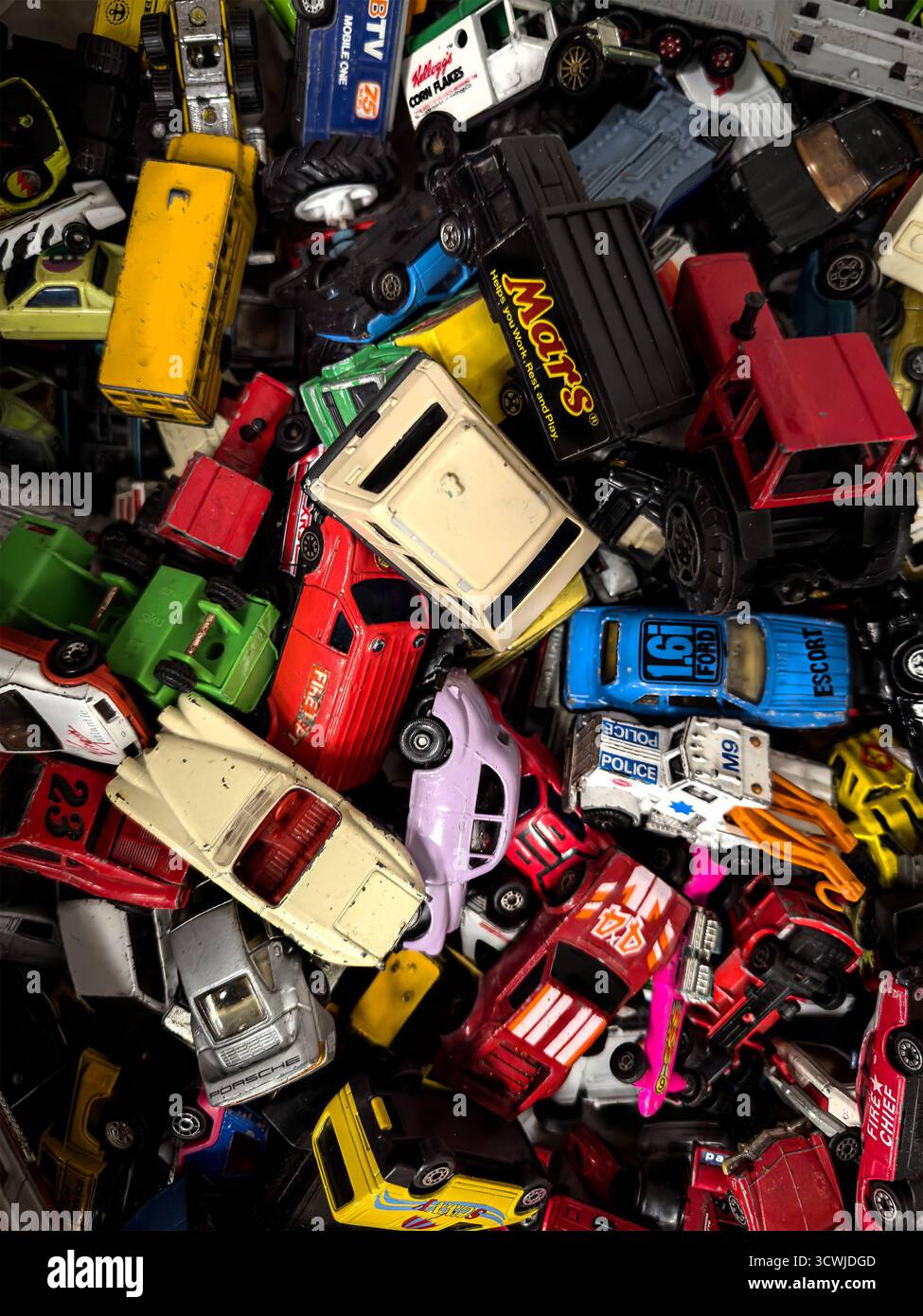 Una caotica pila di colorate macchinine di plastica vintage e di giocattoli pressofusi, veicoli della polizia, camion e vari altri modelli, visti dall'alto con un'illuminazione brillante Foto Stock