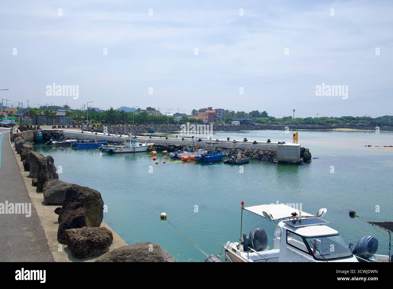 Le barche da pesca ormeggiano in un piccolo porto accanto alla strada costiera vicino alla spiaggia di Shinheung, protetta da una bassa frangiflutti e da una banchina di basalto. Foto Stock