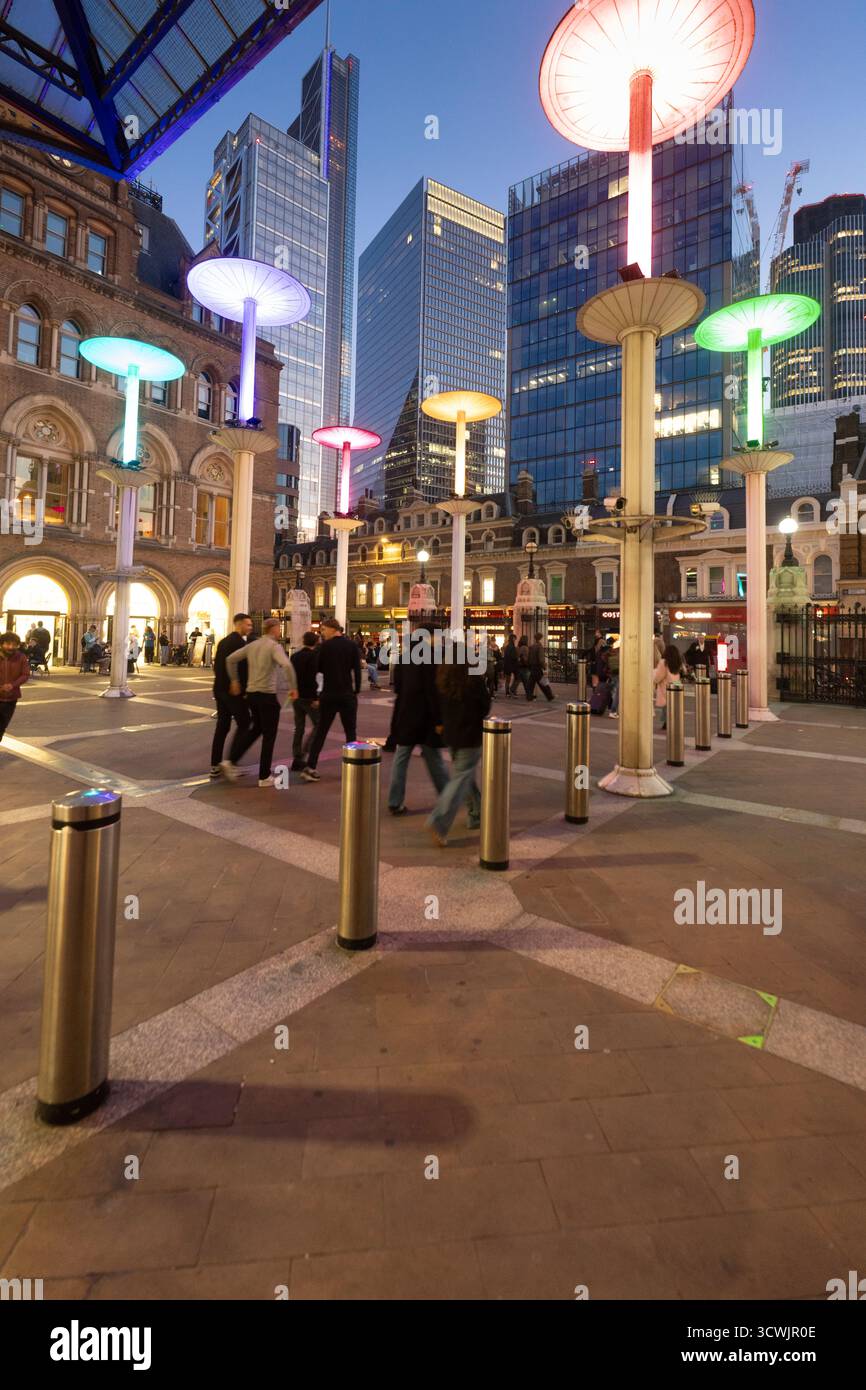 Le persone camminano davanti a sculture illuminate simili a funghi fuori dalla stazione di Liverpool Street, Londra, al crepuscolo. Foto Stock