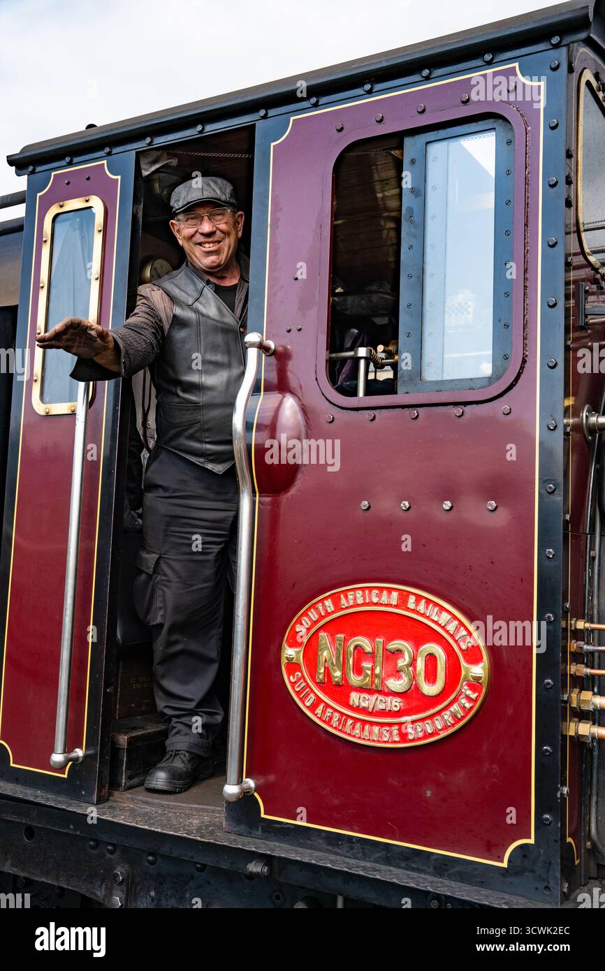 Allegro macchinista in una locomotiva a vapore d'epoca che sfreccia dalla carrozza ferroviaria tradizionale Foto Stock