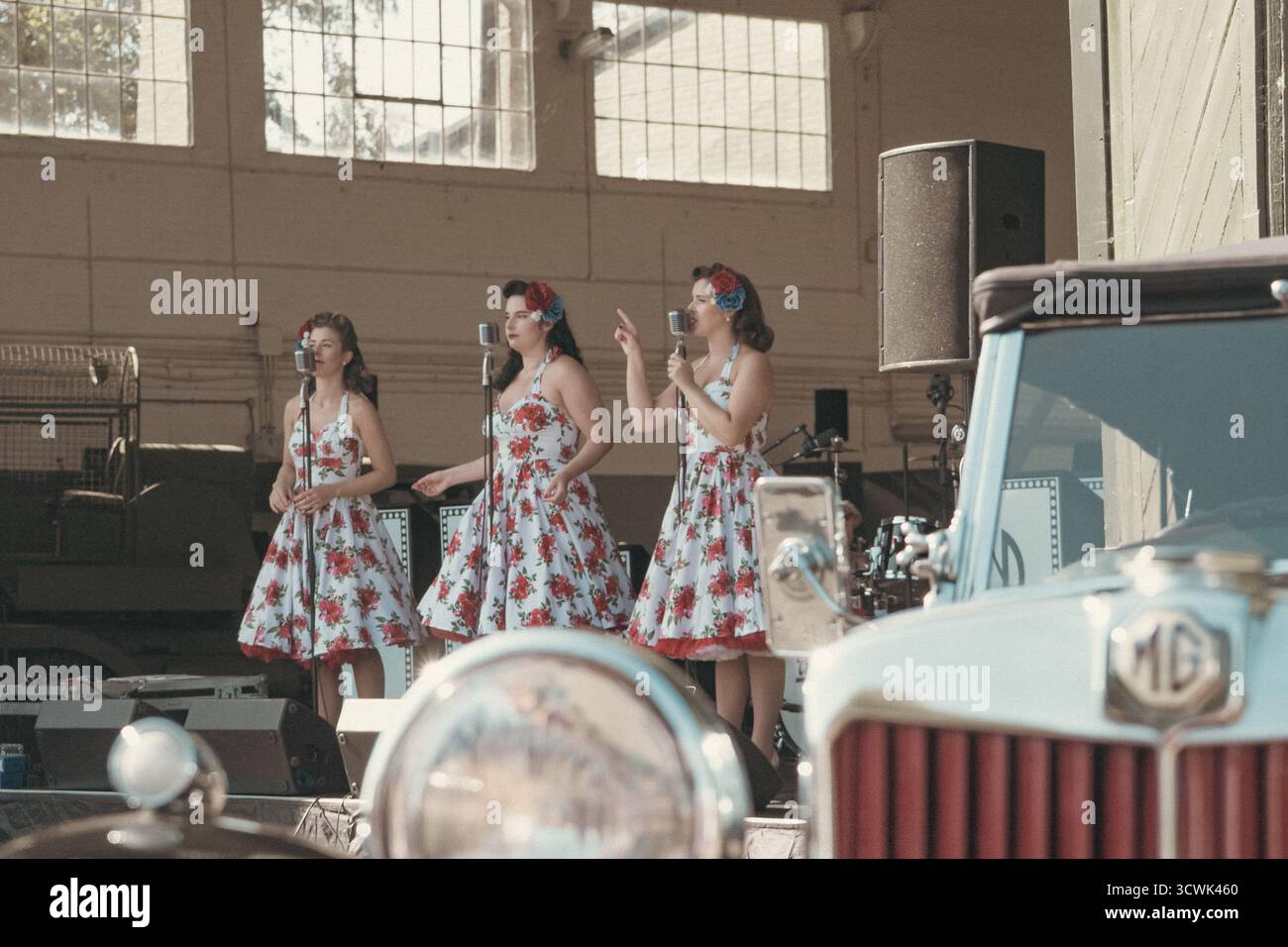 Tre cantanti in abiti floreali d'epoca che si esibiscono nell'hangar storico del museo dell'aviazione Foto Stock