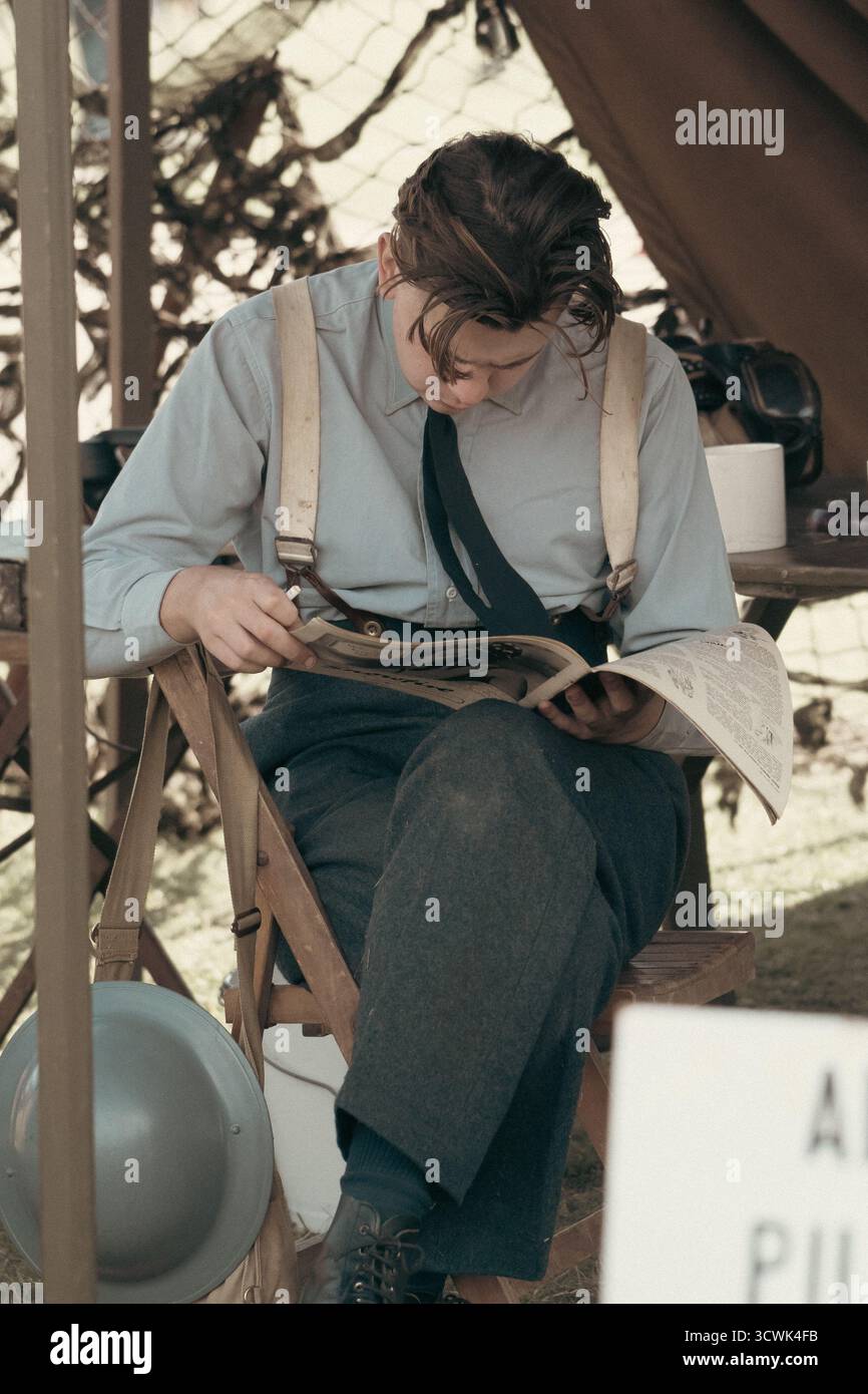 Donna in costume d'epoca che legge il giornale durante l'evento di rievocazione in tempo di guerra Foto Stock