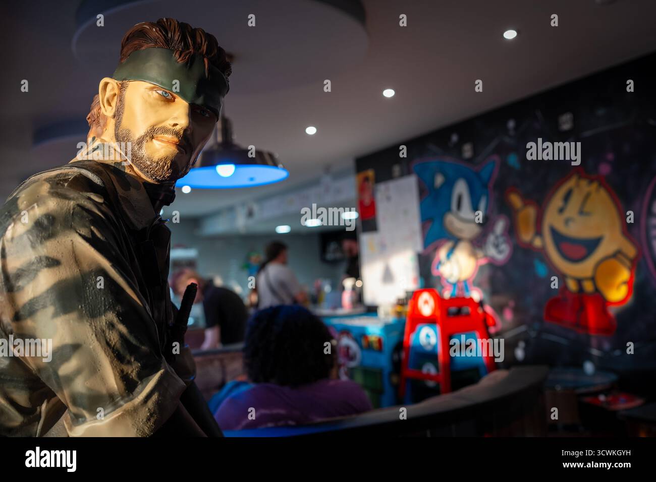 Un personaggio di Metal Gear Solid viene mostrato in una sala giochi retrò con le pareti di Sonic the Hedgehog e PAC-Man Foto Stock