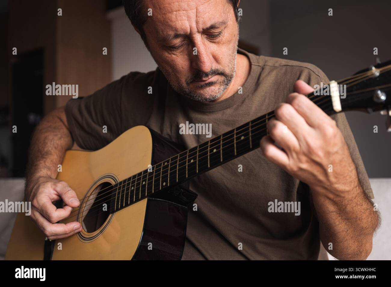 Uomo adulto maturo amatoriale che pratica la chitarra acustica a casa in salotto, musica autodidatta. Messa a fuoco selettiva. Foto Stock