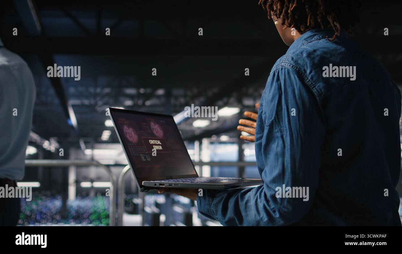 Lo sviluppatore di software per data center si prende il panico dopo aver ricevuto un messaggio di errore critico sul display del notebook. Donna afroamericana nel server hub avvisata da bug che causano basse prestazioni hardware, Foto Stock