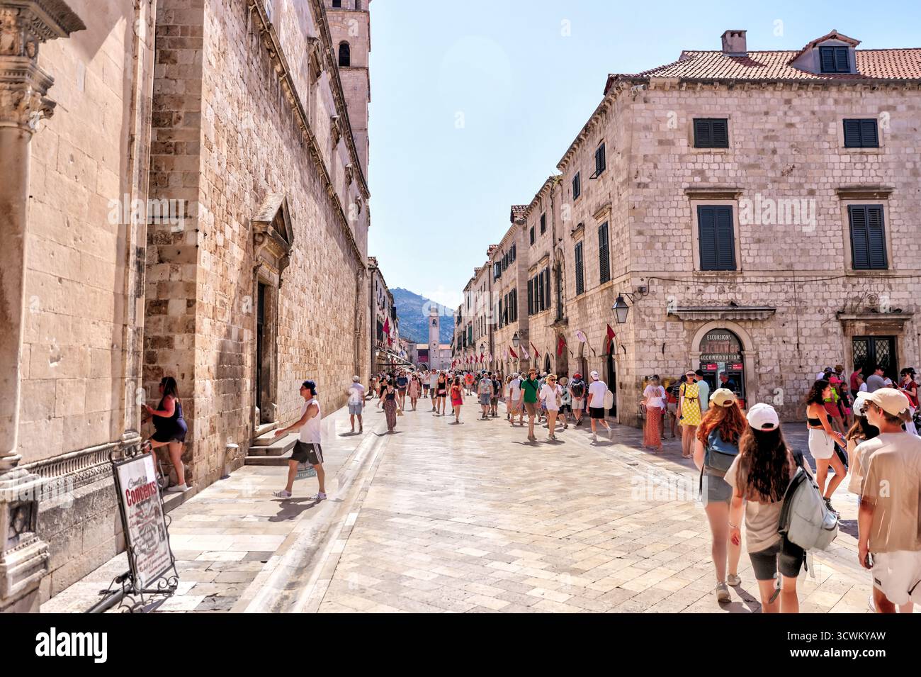 I turisti passeggiano lungo le eleganti strade calcaree di Stradun, la principale via pedonale della città vecchia di Dubrovnik Foto Stock