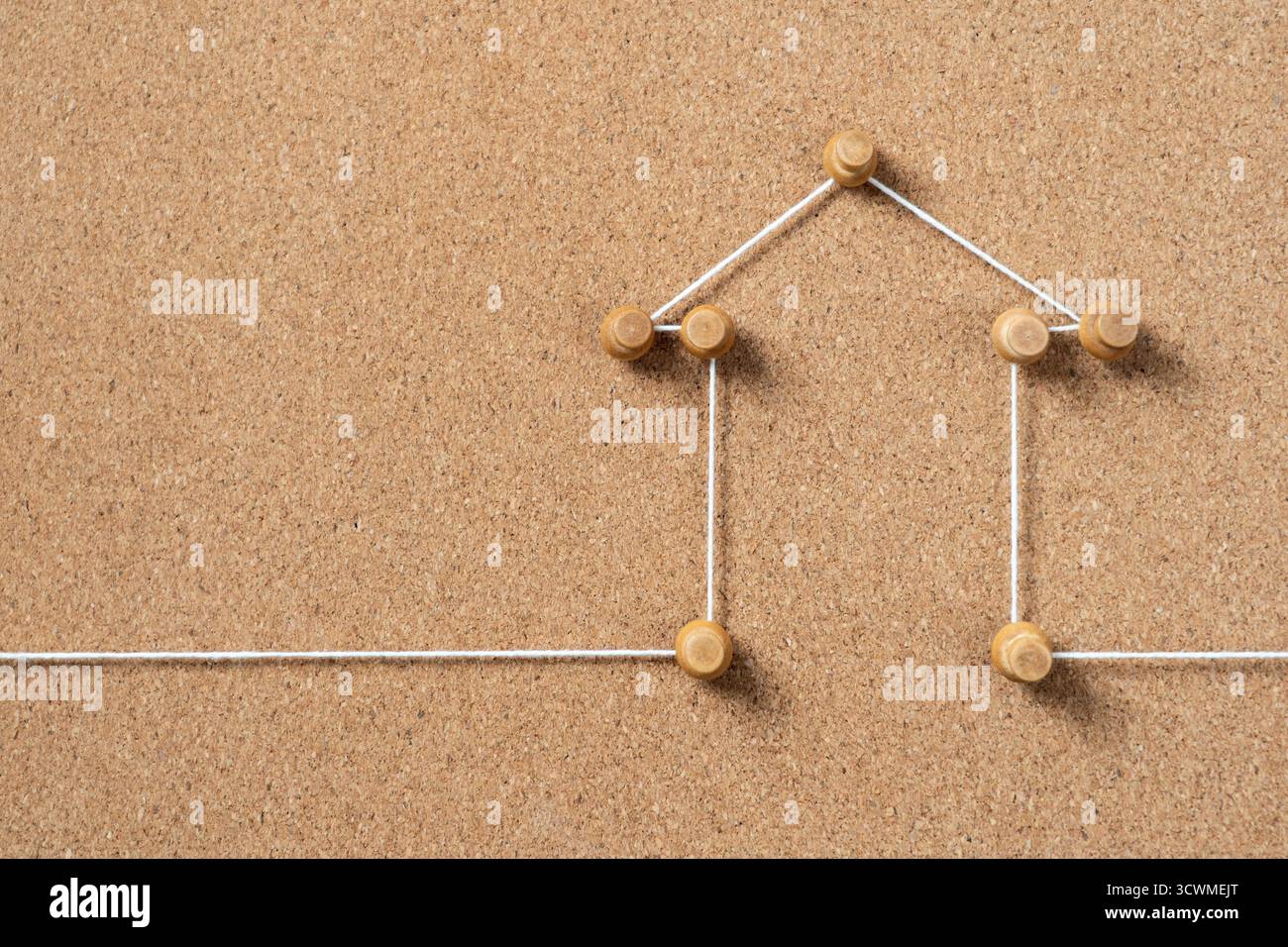 Una rappresentazione minimalista di una casa creata con piccoli spinotti in legno e cordoncino bianco su un cortoncino marrone, che simboleggia casa, proprietà immobiliari o con Foto Stock