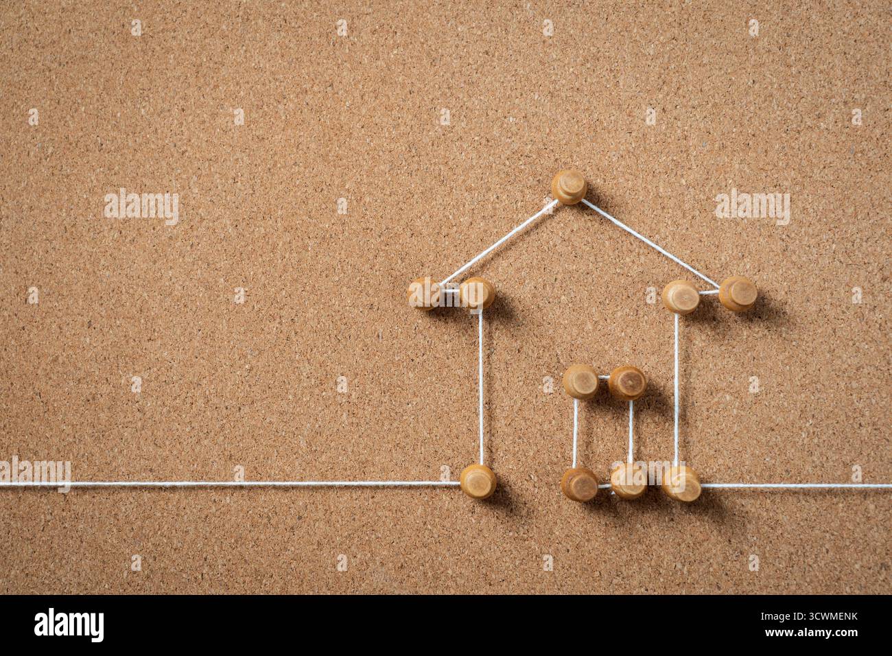 Una rappresentazione minimalista di una casa creata con piccoli spinotti in legno e cordoncino bianco su un cortoncino marrone, che simboleggia casa, proprietà immobiliari o con Foto Stock