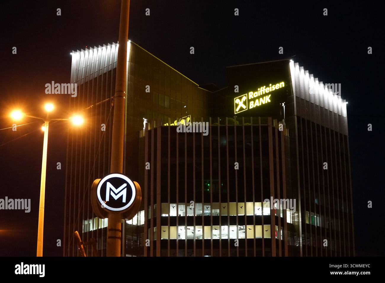 La sede della Raiffeisen Bank illuminata di notte a Budapest, vicino a un ingresso della metropolitana, simboleggia il moderno settore finanziario ungherese. Foto Stock