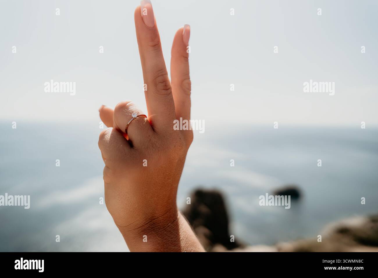 Una mano con un anello solleva due dita in aria su uno sfondo sfocato Foto Stock