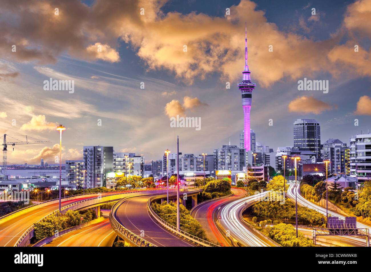Auckland Motorway con percorsi leggeri dal traffico serale, una vista sul CBD con la Sky Tower e un Sunset Sky. Foto Stock