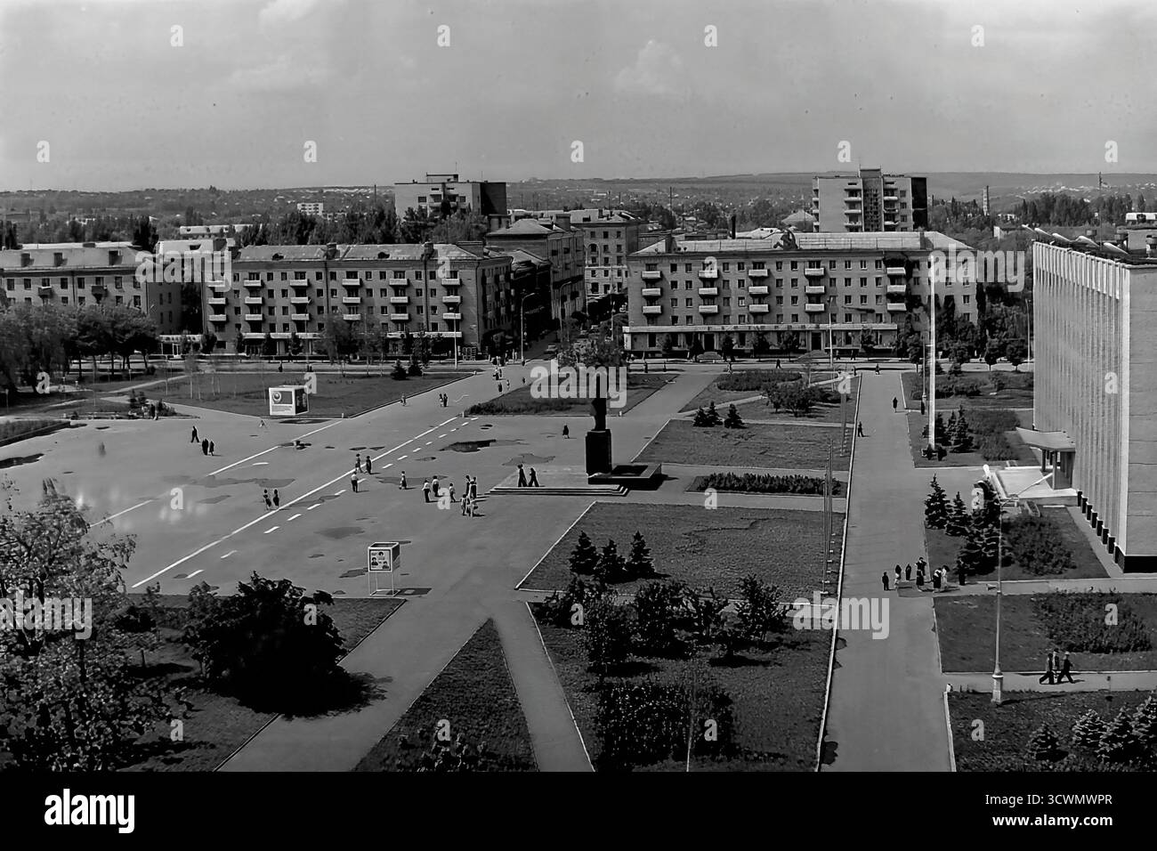 Una vasta vista panoramica ad alto angolo cattura la piazza amministrativa principale di Sloviansk, RSS Ucraina, negli anni '1980 La scena mostra l'ampia Piazza della Rivoluzione d'ottobre (ora Piazza Soborna), un ottimo esempio di pianificazione urbana sovietica, con il monumento centrale a Vladimir Lenin come punto focale. La piazza è circondata da edifici amministrativi e residenziali, verde paesaggistico e ampi sentieri con pochi pedoni, che sottolineano la grande scala. Questa foto documenta il cuore ufficiale e ideologico di una tipica città provinciale della tarda URSS Foto Stock