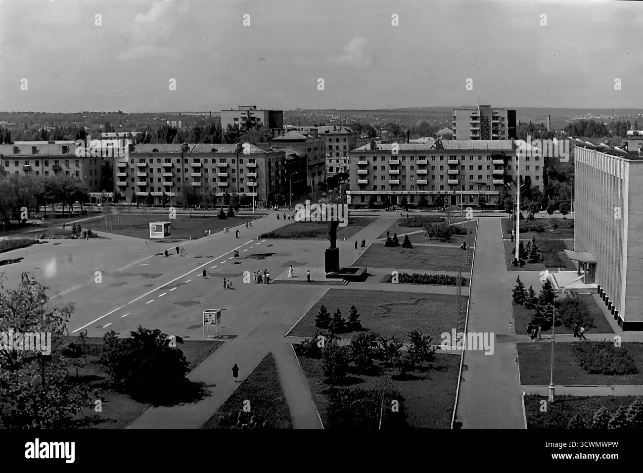 Una vasta vista panoramica ad alto angolo cattura la piazza amministrativa principale di Sloviansk, RSS Ucraina, negli anni '1980 La scena mostra l'ampia Piazza della Rivoluzione d'ottobre (ora Piazza Soborna), un ottimo esempio di pianificazione urbana sovietica, con il monumento centrale a Vladimir Lenin come punto focale. La piazza è circondata da edifici amministrativi e residenziali, verde paesaggistico e ampi sentieri con pochi pedoni, che sottolineano la grande scala. Questa foto documenta il cuore ufficiale e ideologico di una tipica città provinciale della tarda URSS Foto Stock