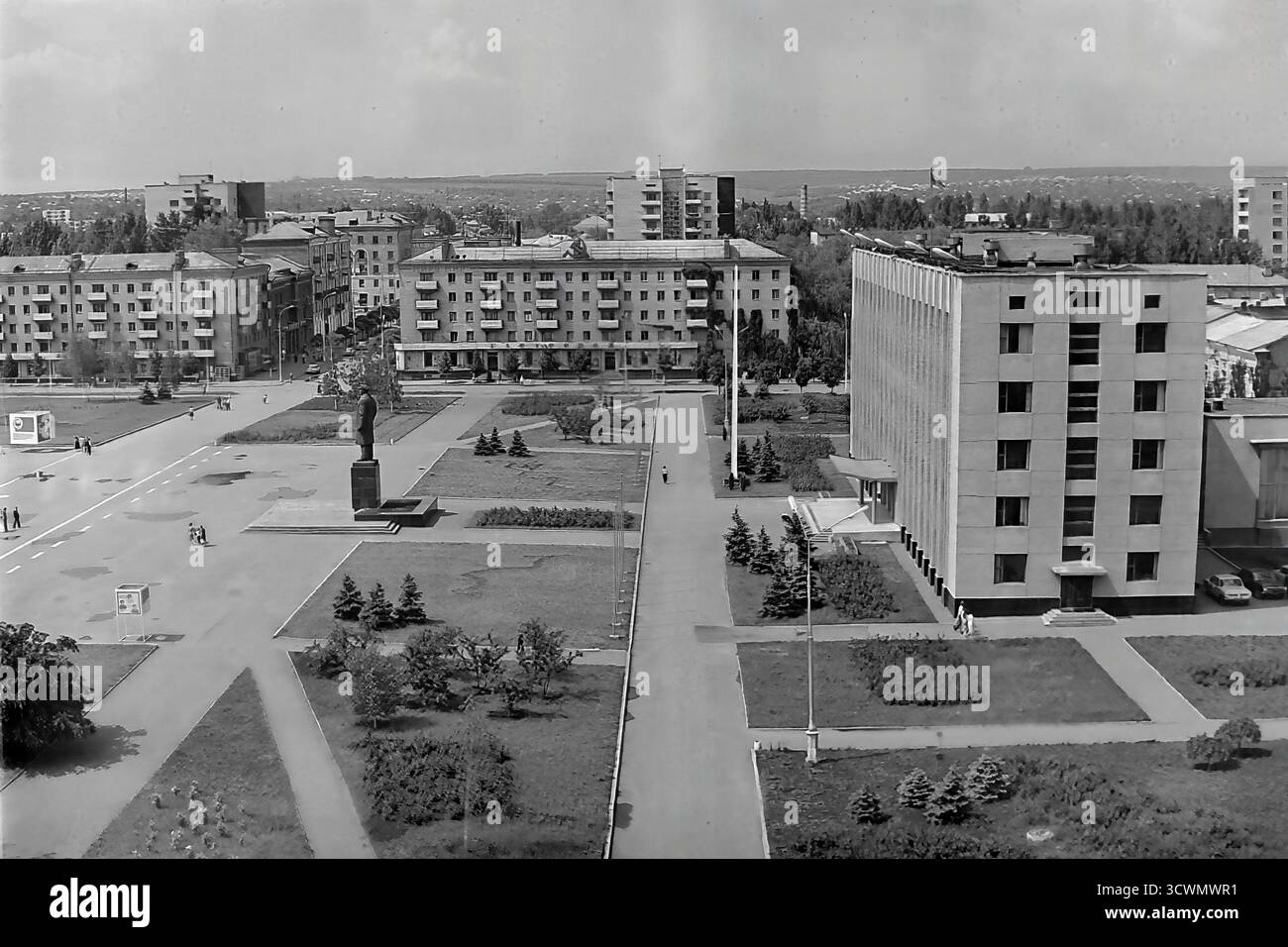 Una vasta vista panoramica ad alto angolo cattura la piazza amministrativa principale di Sloviansk, RSS Ucraina, negli anni '1980 La scena mostra l'ampia Piazza della Rivoluzione d'ottobre (ora Piazza Soborna), un ottimo esempio di pianificazione urbana sovietica, con il monumento centrale a Vladimir Lenin come punto focale. La piazza è circondata da edifici amministrativi e residenziali, verde paesaggistico e ampi sentieri con pochi pedoni, che sottolineano la grande scala. Questa foto documenta il cuore ufficiale e ideologico di una tipica città provinciale della tarda URSS Foto Stock