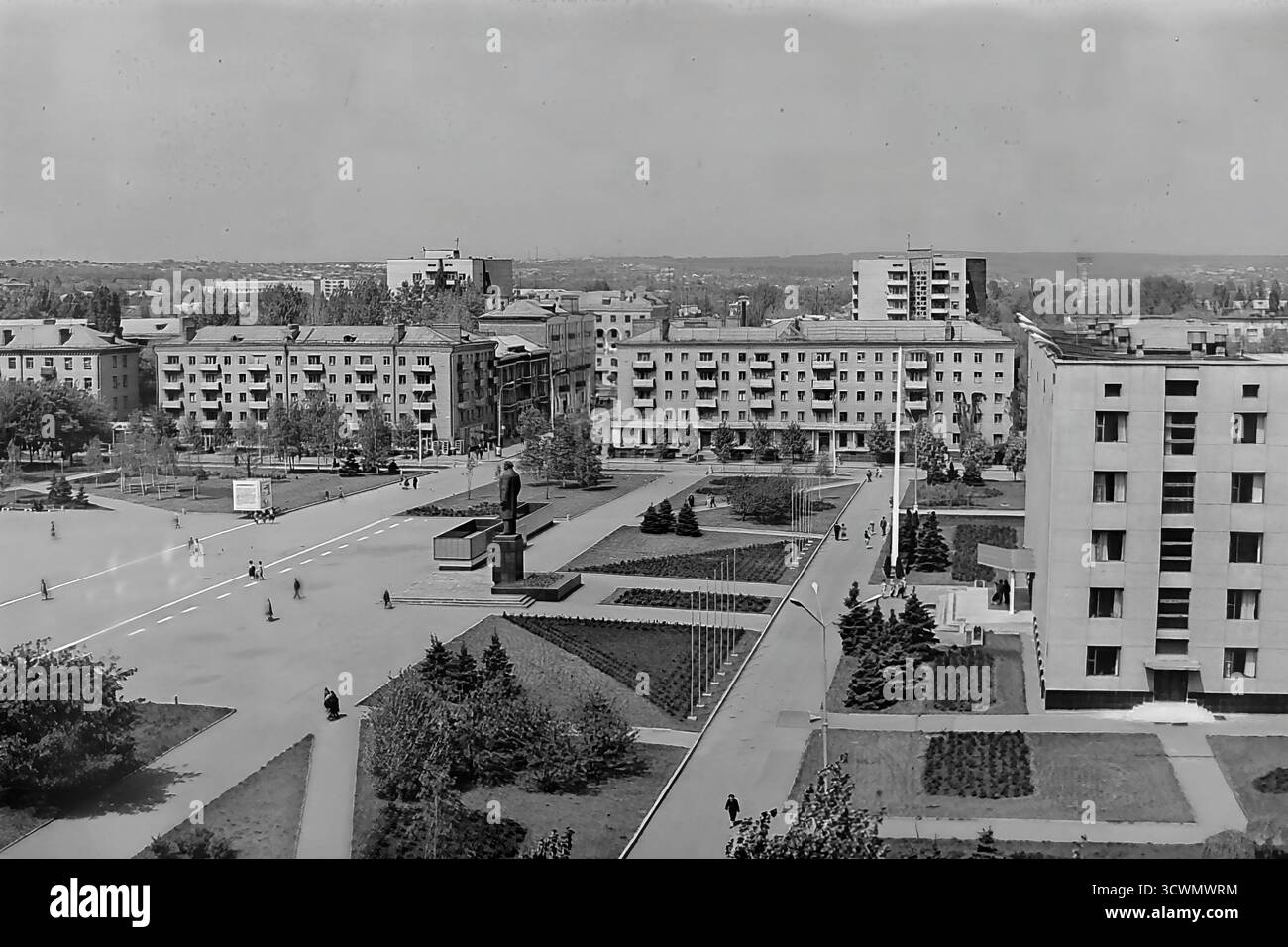 Una vasta vista panoramica ad alto angolo cattura la piazza amministrativa principale di Sloviansk, RSS Ucraina, negli anni '1980 La scena mostra l'ampia Piazza della Rivoluzione d'ottobre (ora Piazza Soborna), un ottimo esempio di pianificazione urbana sovietica, con il monumento centrale a Vladimir Lenin come punto focale. La piazza è circondata da edifici amministrativi e residenziali, verde paesaggistico e ampi sentieri con pochi pedoni, che sottolineano la grande scala. Questa foto documenta il cuore ufficiale e ideologico di una tipica città provinciale della tarda URSS Foto Stock