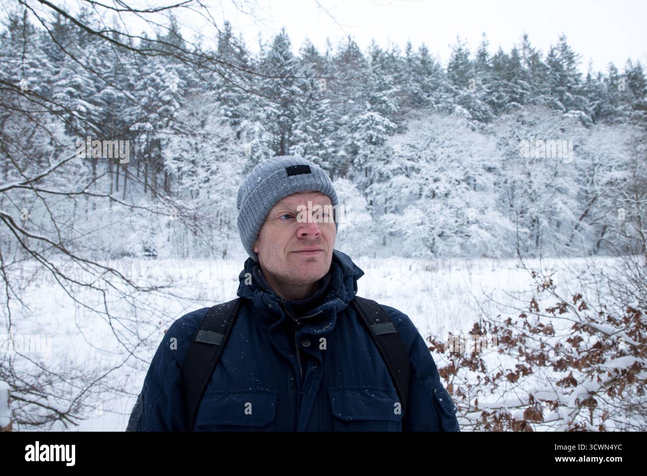 ritratto uomo maturo in inverno con foresta dietro coperta di neve, uomo con berretto e giacca invernale primo piano ritratto, gente comune Foto Stock
