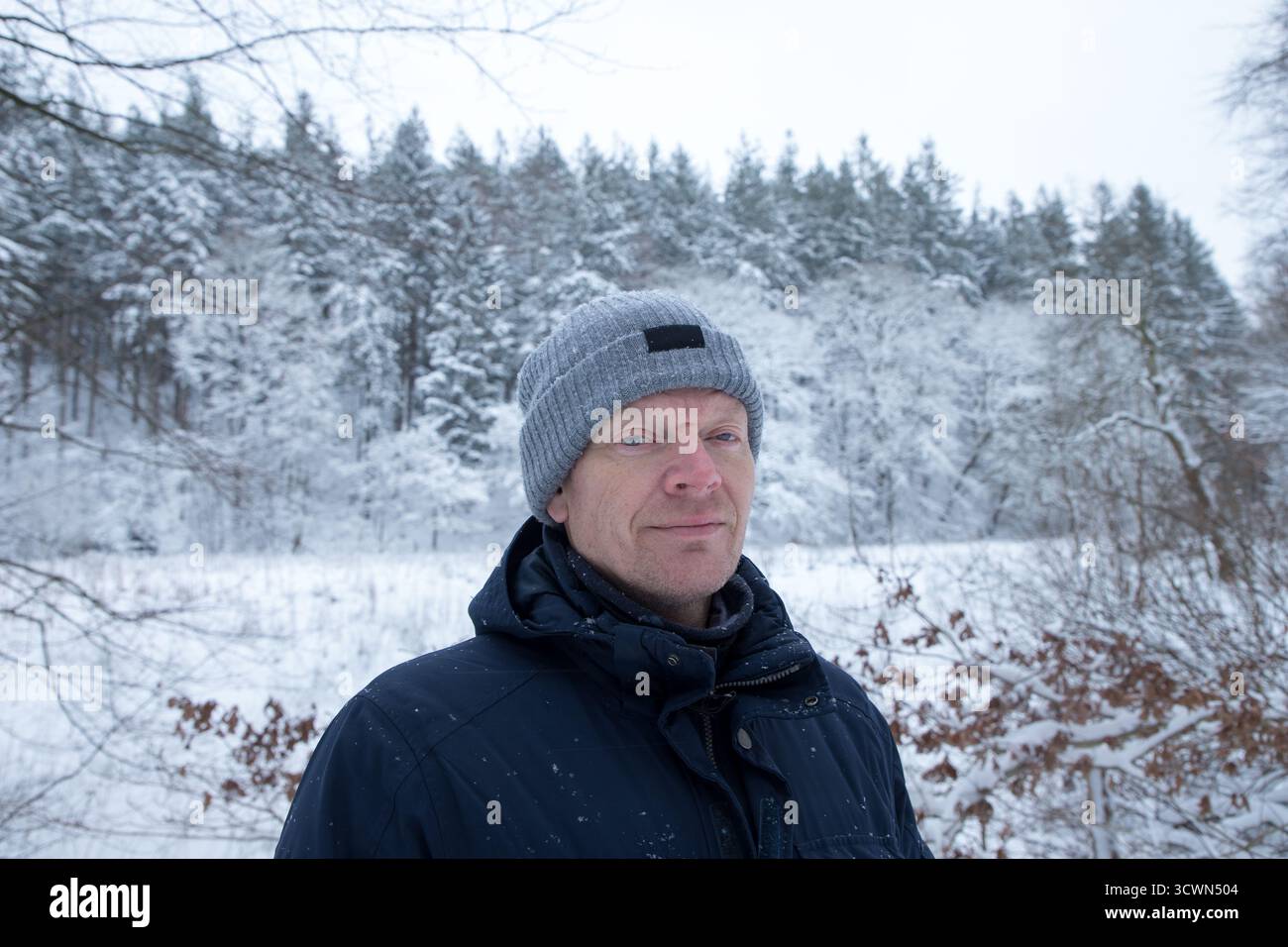 ritratto uomo maturo in inverno con foresta dietro coperta di neve, uomo con berretto e giacca invernale primo piano ritratto, gente comune Foto Stock