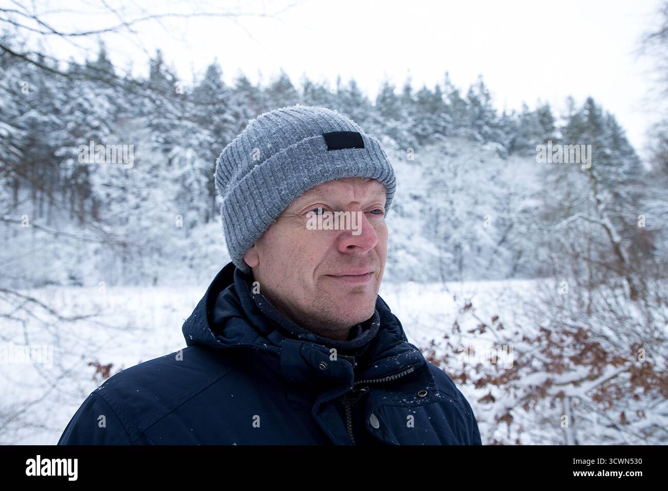 ritratto uomo maturo in inverno con foresta dietro coperta di neve, uomo con berretto e giacca invernale primo piano ritratto, gente comune Foto Stock