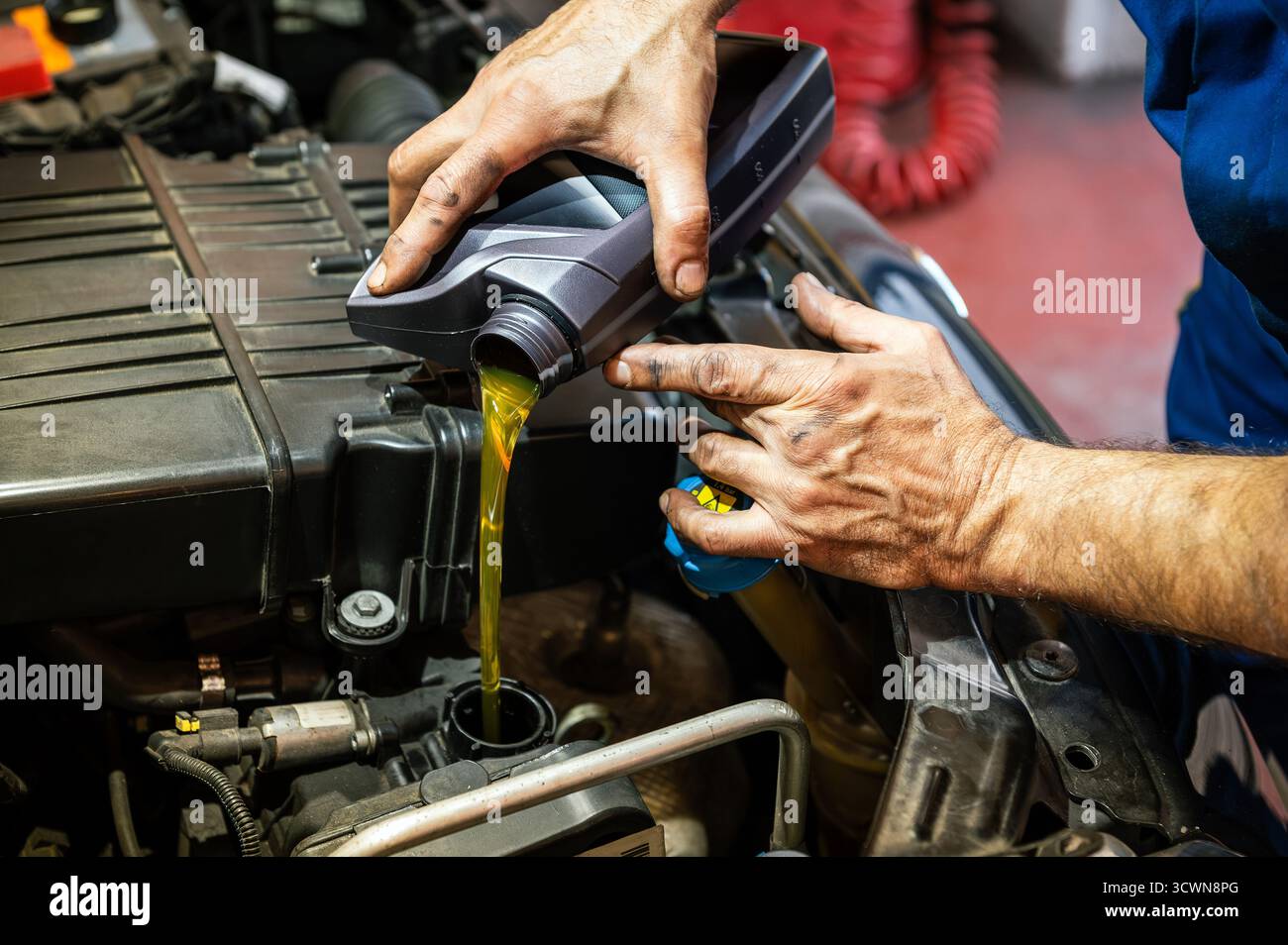 Mani del meccanico che versano olio motore da una bottiglia nel motore di un'auto Foto Stock